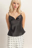 Woman wearing a black satin camisole and polka dot skirt on a plain background