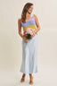 Woman wearing a colorful sleeveless top and light blue skirt holding flowers against a plain background