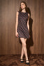 A woman modeling a sleeveless, knee-length A-line dress with a dark navy and red geometric pattern, standing against a brown wood-paneled wall.