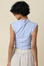 Person wearing a light blue sleeveless top with a beige background