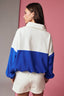 Woman wearing a white and blue color-blocked sweater against a pink background