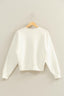 White sweater on a wooden hanger against a beige wall