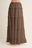 A brown tiered maxi skirt with ruffled trim, shown on a model against a plain beige background.