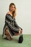 Woman wearing a black and white striped dress, kneeling on a green floor with a plain background