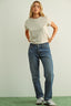 Woman wearing a light gray t-shirt and blue jeans standing against a plain background