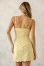 Woman wearing a light yellow dress with thin straps against a neutral background