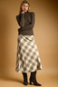 Woman wearing a brown ribbed sweater and plaid skirt against a beige background