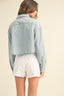 Person wearing a light blue denim jacket and white shorts on a beige background