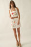 Woman wearing a white sleeveless top and skirt with floral embroidery on a plain background