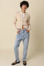 Woman wearing a beige cardigan, white shirt, light blue jeans, and black flats on a beige background