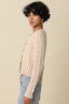 Woman wearing a beige cable knit sweater and light blue jeans against a beige background