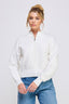 Woman wearing a white zip-up sweater and blue jeans against a plain background