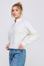 Woman wearing a white ribbed sweater and blue jeans on a light gray background
