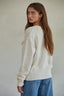Woman wearing a cream sweater and blue jeans against a plain background
