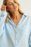 Woman wearing a light blue button-up shirt with a neutral background