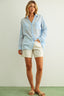 Woman wearing a light blue checkered shirt and white shorts on a plain background