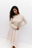 Woman wearing a beige sweater over a white dress against a white background