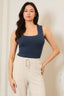 Woman wearing a navy tank top and beige pants against a plain background