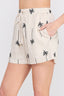 Beige shorts with palm tree pattern worn by a person on a white background