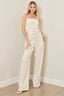 Woman wearing a beige strapless jumpsuit against a plain wall.
