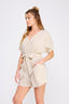 Woman wearing a beige romper with a belt on a white background