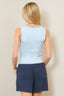 Woman wearing a light blue sleeveless top and navy shorts against a beige background