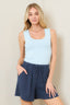 Woman wearing a light blue tank top and navy shorts against a beige background