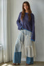 Woman wearing a blue sweater and patterned pants standing in a room with curtains.