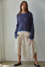 Woman wearing a blue sweater and white lace skirt against a plain background