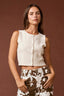 Woman wearing a white sleeveless top and patterned pants on a brown background