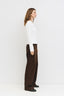 Woman wearing a white top and brown pants standing against a white background