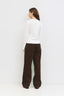 Person wearing a white top and brown pants against a white background