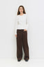 Woman wearing a white sweater and brown pants on a white background