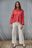 Woman wearing a red cable knit sweater and white pants against a gray background