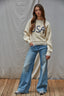 Person wearing a cream sweater with 'USA' text and blue jeans against a plain background