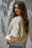 Woman wearing a cream-colored sweater against a textured white wall