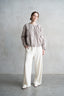 Woman wearing a beige blouse and white pants against a gray background