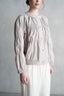 Person wearing a beige blouse with long sleeves and a white skirt against a plain background