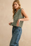 Woman wearing a green knitted sleeveless top and blue jeans against a beige background