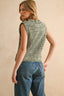 Woman wearing a sleeveless green knitted top and blue jeans against a beige background