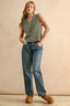 Woman wearing a green sleeveless top and blue jeans against a beige background