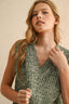 Woman wearing a green patterned sleeveless top against a beige background
