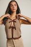 Woman wearing a sleeveless top with brown accents against a neutral background