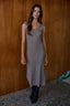 Woman wearing a sleeveless, knee-length dress against a wooden wall.