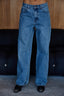 Blue jeans worn by a person standing against a wooden wall.