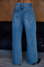 Blue jeans worn by a person standing against a wooden wall.