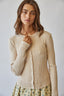 Woman wearing a beige ribbed sweater over a floral dress against a plain background