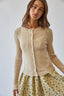Woman wearing a beige ribbed cardigan over a floral dress against a white background