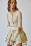 Woman wearing a beige ribbed sweater and floral skirt on a plain background