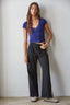 Woman wearing a blue top and black pants with white stripes against a plain background